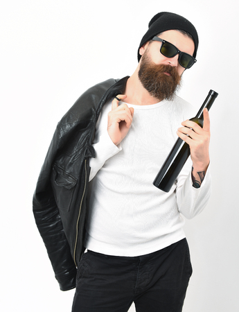 caucasian serious unshaven hipster holding bottle in black leather jacket, hat and glasses isolated on white studio backgroundの写真素材