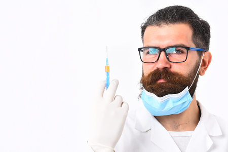 Bearded man, long beard. Brutal caucasian doctor or unshaven hipster, postgraduate student in mask, medical gown and gloves holding syringe isolated on white studio background. Medicine conceptの写真素材