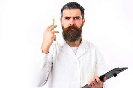 Bearded man, long beard. Brutal caucasian doctor or unshaven hipster, postgraduate student holding clipboard with syringe in medical gown isolated on white studio background. Medicine conceptの写真素材