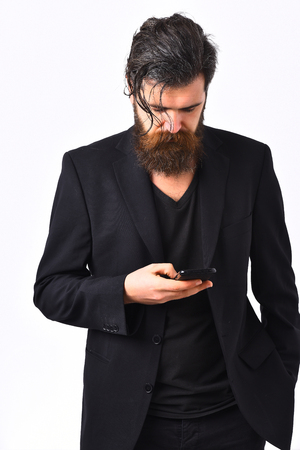 Bearded man, long beard. Brutal caucasian hipster with moustache holding cell phone in black suit isolated on white studio backgroundの写真素材