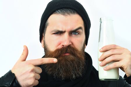 Bearded man, long beard. Brutal caucasian serious unshaven hipster shows on glass jar of milk in...