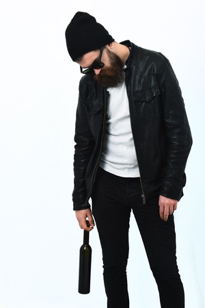 Bearded man, long beard. Brutal caucasian serious unshaven hipster holding bottle in black leather jacket, hat and glasses isolated on white studio backgroundの写真素材