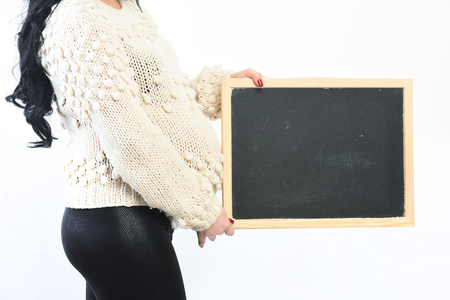 female hands of pregnant woman holding black board in beige knitted sweater isolated on white studio background, copy spaceの写真素材