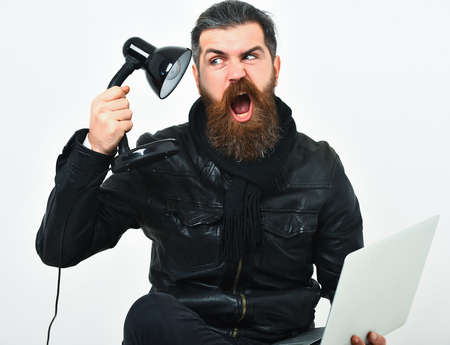 Bearded man, long beard. Brutal caucasian crazy unshaven hipster sitting and holding laptop with lamp in black leather jacket isolated on white studio backgroundの写真素材
