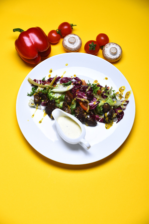 cooked meat, fresh salad leaves, mustard and sauce on white plate, red sweet pepper near silver knife, pepperbox and saltcellar, cherry tomato, mushroom on grey background with burlapの写真素材
