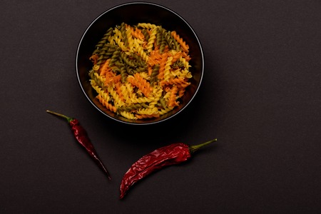 Colorful dried fusilli, italian pasta in bowl plate, with chilly pepper, for cooking vegetarian food on black background, copy spaceの写真素材