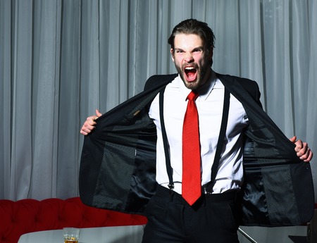 bearded man, businessman, long beard, brutal caucasian hipster with moustache has angry shouting face, unshaven guy with stylish hair in suit and red tie against curtainsの写真素材