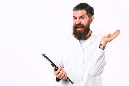 Bearded man, long beard. Brutal caucasian doctor or happy smiling unshaven hipster, postgraduate student holding clipboard and pills in gown isolated on white studio background. Medicine conceptの写真素材