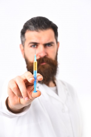 Bearded man, long beard. Brutal caucasian doctor or unshaven hipster, postgraduate student holding syringe in medical gown isolated on white studio background. Medicine conceptの写真素材