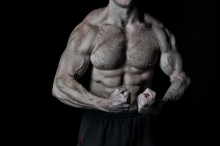 handsome bodybuilder man or sexy muscular guy with athlete body, torso and chest training sport and posing in gym on black background, copy spaceの写真素材