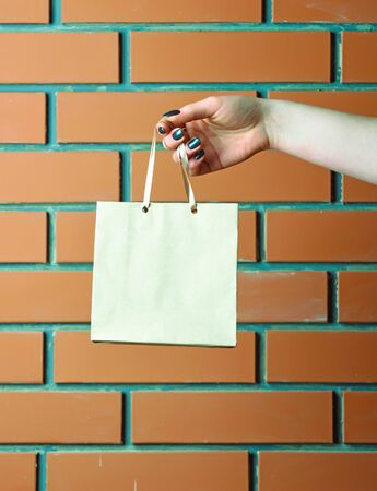 white color paper shopping bag or package in female hand as holiday present or gift on brick wall background, copy spaceの写真素材