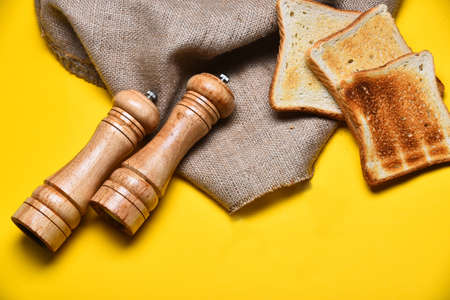 fried toast bread, wooden saltcellar, pepperbox and burlap on yellow background, copy spaceの写真素材