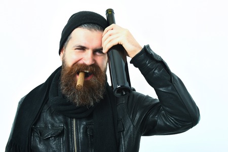 Bearded man, long beard. Brutal caucasian smiling happy unshaven hipster holding bottle and smoking cigar in black leather jacket, hat and scarf isolated on white studio backgroundの写真素材