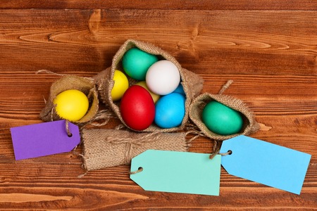 easter colorful eggs painted in bright colors in burlap sack on brown wood on wooden background with...