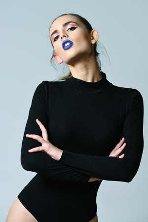 Pretty girl or sexy woman, slim fashion model, with adorable face, blue lips, stylish makeup, long hair, ponytail, in sexi, black bodysuit on grey backgroundの写真素材