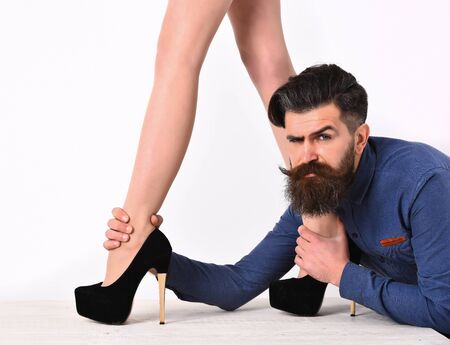 bearded man, long beard, brutal caucasian hipster with moustache on serious face with female sexy legs in fashionable shoes isolated on white background getting haircut in blue shirtの写真素材
