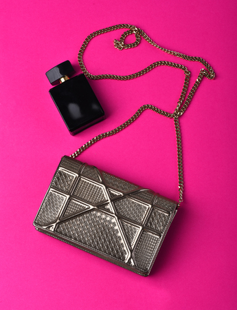 Nice beautiful small womans metallized silver fashionable bag with decorative metallic chain near perfume on pink backgroundの写真素材