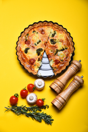 pizza or vegetable pie, fresh red cherry tomato, mushroom, rosemary, salt, pepper spice on tray near pepperbox, saltcellar on yellow backgroundの写真素材