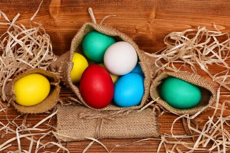 easter colorful eggs painted in bright colors in burlap sack with straw on wooden background, spring holiday celebrationの写真素材