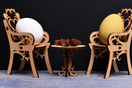 easter egg in wooden chairs at table with badian or star anise spice in dining room on grey wood and black background, spring holiday celebrationの写真素材