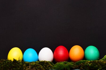 easter colorful eggs painted in bright colors in line or row on black background with green moss, spring holiday celebration, copy spaceの写真素材