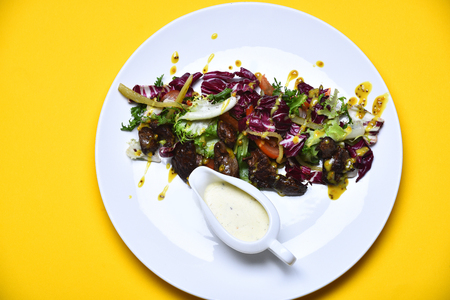 cooked meat, fresh salad leaves, mustard and sauce on white plate on yellow backgroundの写真素材