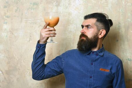 Bearded man, long beard. Brutal caucasian serious hipster with moustache in blue denim shirt holding alcoholic fresh cocktail on texture backgroundの写真素材