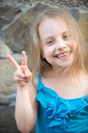 small baby happy girl or cute child with adorable smiling face and blonde long hair in blue dress in summer outdoor on stony wall backgroundの写真素材
