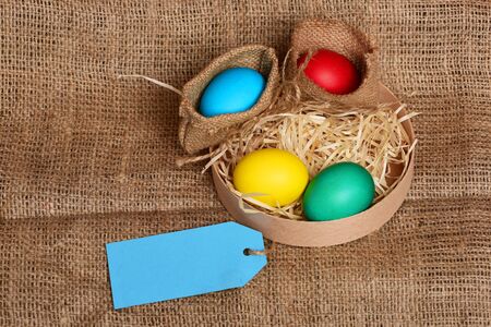 easter colorful eggs painted in bright colors in burlap sack and wooden box with straw and blue...