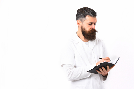 Bearded man, long beard. Brutal caucasian doctor or unshaven hipster, postgraduate student holding notebook with pen in medical gown isolated on white studio background. Medicine conceptの写真素材