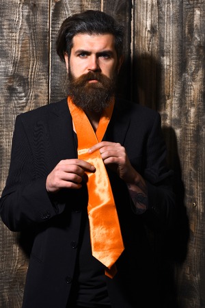 Bearded man, long beard. Brutal caucasian hipster with moustache have acid orange tie on suit on brown vintage wooden studio backgroundの写真素材