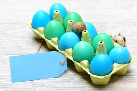 set of traditional eggs painted in bright color inside carton box with tag on grey vintage wooden...