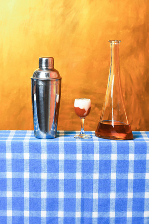 metallic shaker, flask or bottle with alcohol and singapore sling shot with cream on blue checkered...