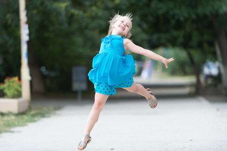 small baby girl or cute happy child with adorable smiling face and bow in blonde hair in blue dress jumping in summer outdoor on blurred backgroundの写真素材