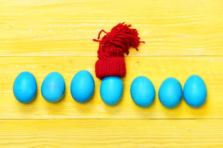 set of traditional eggs painted in blue color in line or row with toy red hat on yellow vintage wooden background. Happy Easter conceptの写真素材