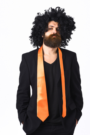 Bearded man, long beard. Brutal caucasian hipster with moustache have acid orange tie on suit and black curly afro wig isolated on white studio backgroundの写真素材