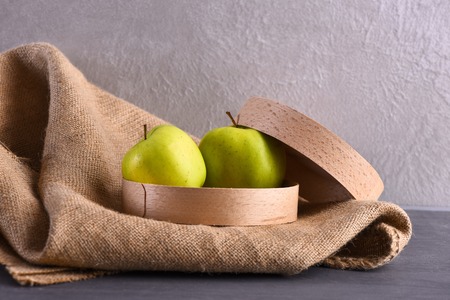 fresh green apples in wooden box on sackcloth napkin, studio wall background, side viewの写真素材