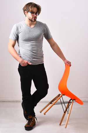 Bearded man, short beard. Caucasian sexy macho with moustache in glasses lean on orange chair posing on studio backgroundの写真素材