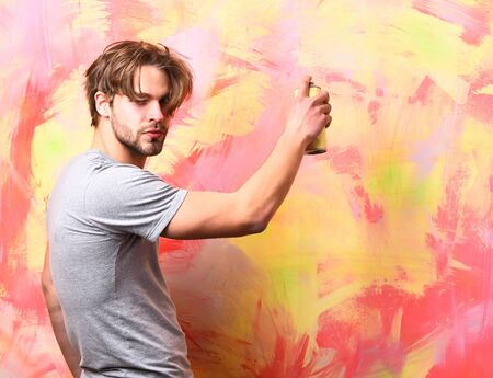 Bearded man, short beard. Caucasian serious macho with moustache wearing gray shirt holding spray paint on colorful studio backgroundの写真素材