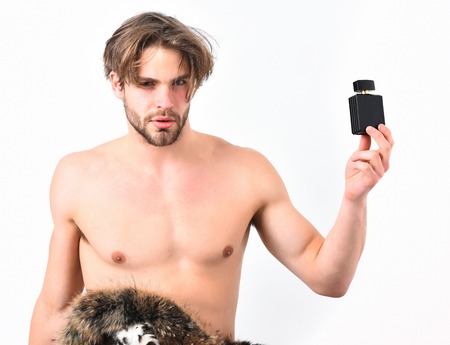 Bearded man, short beard. Caucasian serious macho with moustache enveloped in fur coat showing six packs and abs on muscle torso, holding perfume bottle, isolated on white backgroundの写真素材