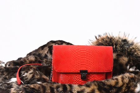 Red stylish female leather handbag on spotted fluffy fur coat background, side view