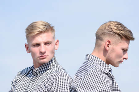 young stylish handsome twins in checkered shirts posing with serious faces on blue sky backgroundの写真素材