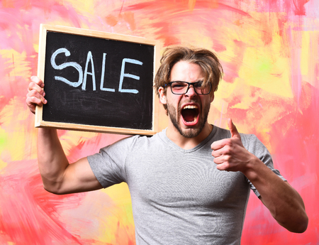 Bearded man, short beard. Caucasian sexy angry macho man with moustache in glasses wearing gray shirt holding black board with sale inscription showing gesture yes on colorful studio backgroundの写真素材