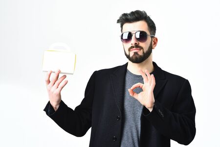 Bearded man, short beard. Caucasian hipster with moustache in sunglasses, holding meal box, wearing black jacket showing ok gesture isolated on white backgroundの写真素材