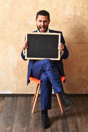 blackboard in hands of confused teacher man or businessman in suit, empty chalkboard for copy spaceの写真素材