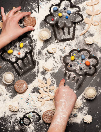 Drawn flour muffins. Female hands drawing muffins on flour spread on the black table, filled with chocolate cookies, colorful sweets and wooden decorations making artistic pattern. Homemade conceptの写真素材