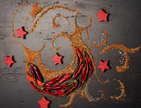 Spicy abstract art piece made of different asian spices, red wooden stars and chili peppers on black...
