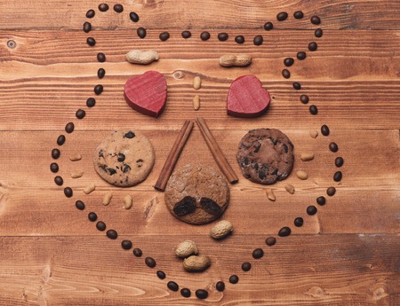 Bear face made of cookies, biscuits, red candy hearts, coffee beans, raisins and nuts on warm...