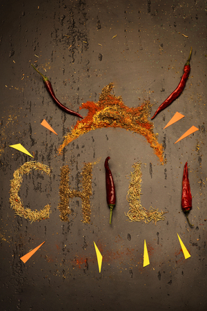 Chili peppers and spices. Chili word with burning colourful arrows on brown grey backgroundの写真素材