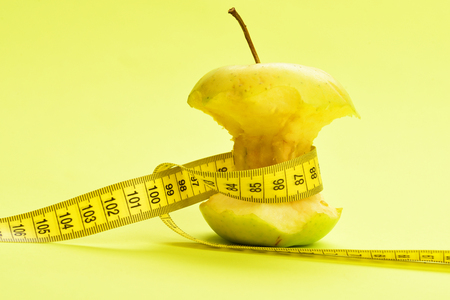 Apple and yellow measure tape which ties it around a on warm yellow background.の写真素材